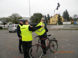 Policjant i strażnik przekazują kamizelkę odblaskową rowerzyście.