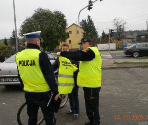 Policjanci i strażnik przekazują kamizelkę odblaskową rowerzyście.