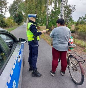 policjantka stoi przy kobiecie prowadzącej rower wręcza jej elementy odblaskowe